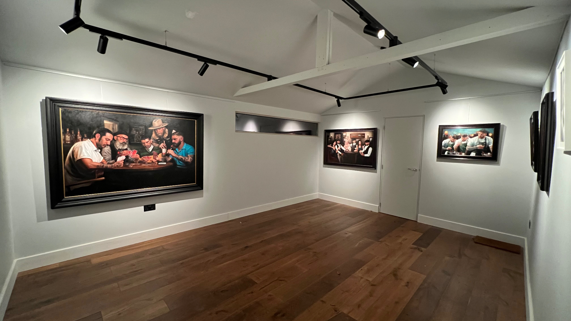 The finished private gallery: a large Vince Kamp painting on the left wall, further framed works beyond, suspended black three circuit track above and a timber floor below.