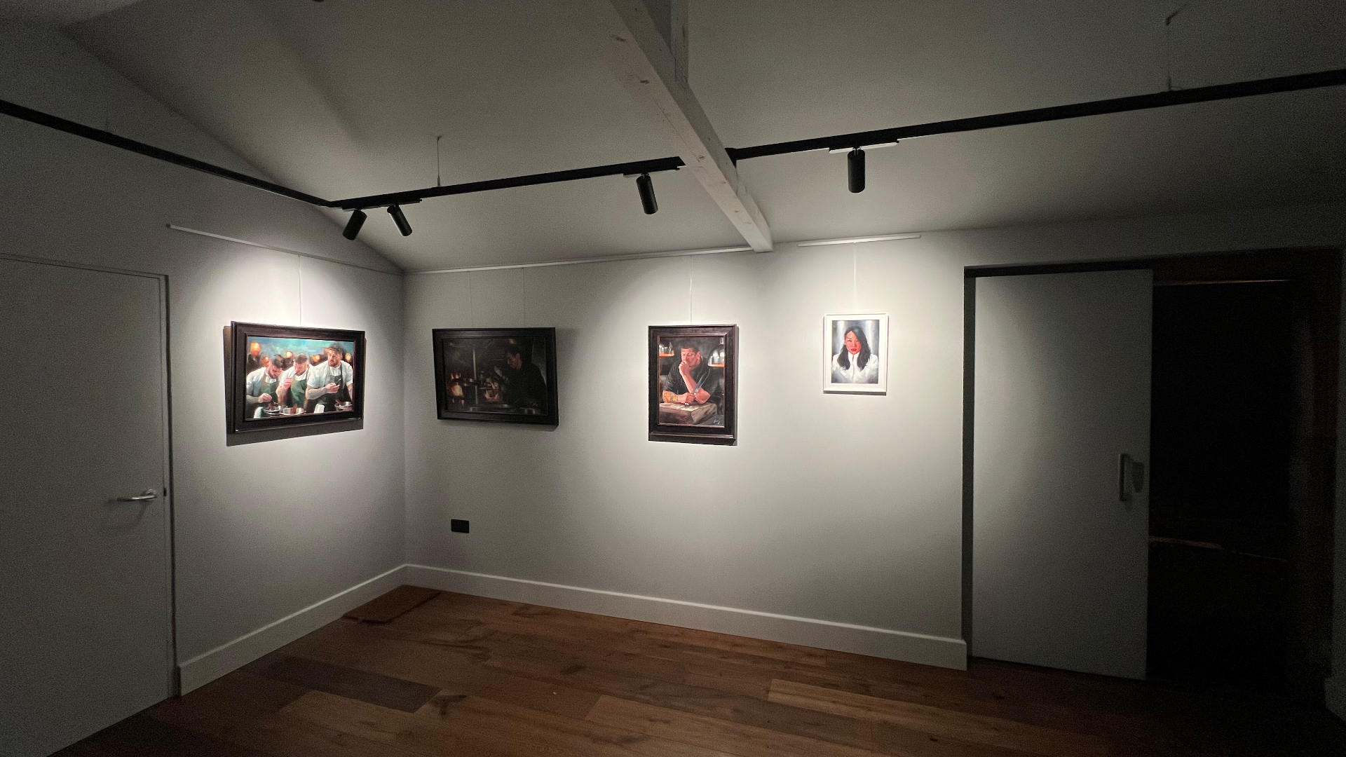 A darker view of the finished gallery, four framed paintings lit precisely while the surrounding walls fall away.