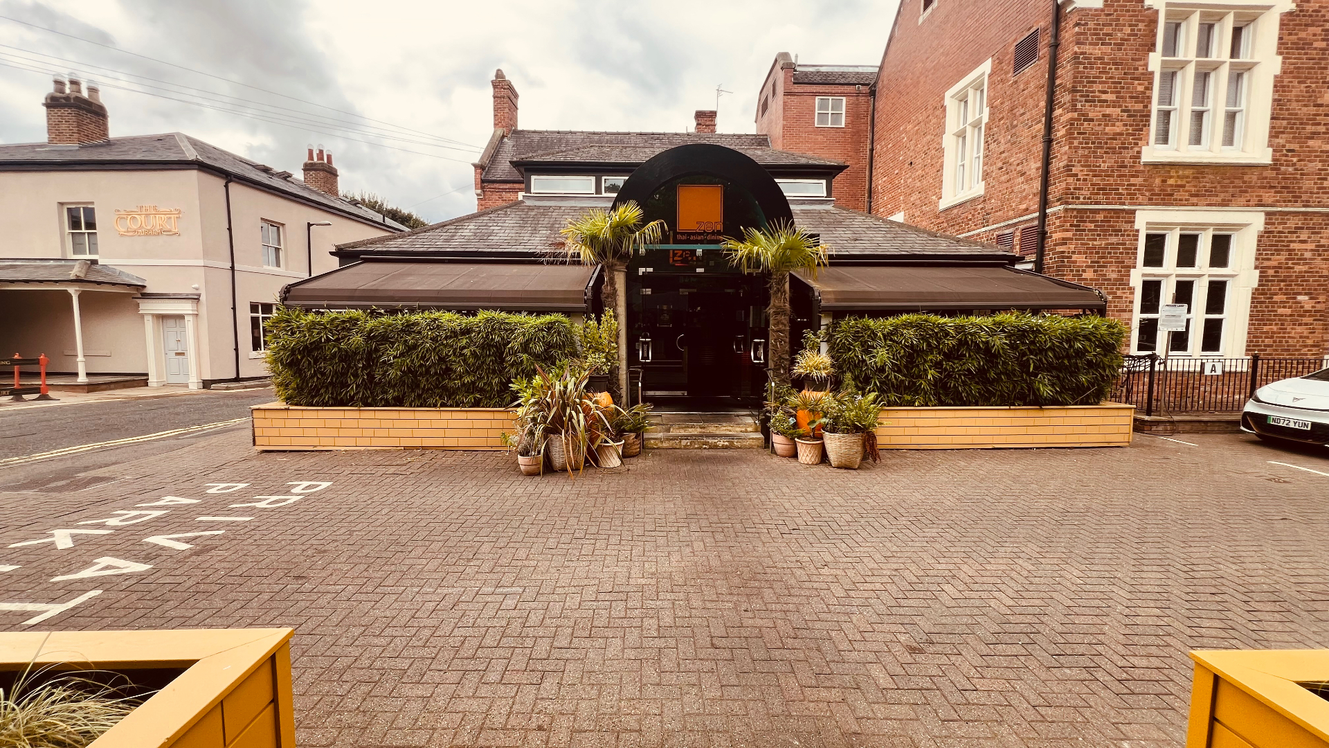 The entrance to Zen with palm trees and dense hedging either side of the doorway.