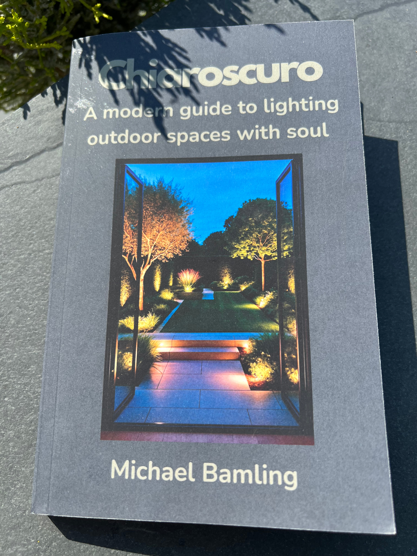 Cover of Chiaroscuro — A Modern Guide to Lighting Outdoor Spaces with Soul, by Michael Bamling: a lit garden seen through open glazed doors at dusk.