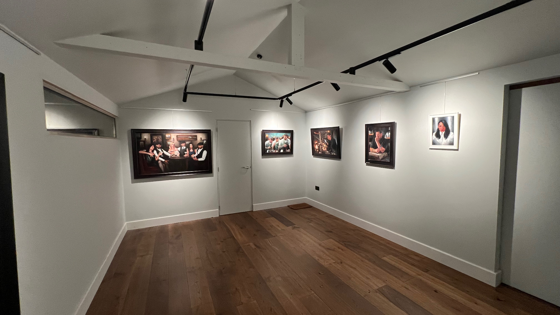 Wide view of the completed gallery with paintings lit individually along two walls beneath the vaulted white ceiling.