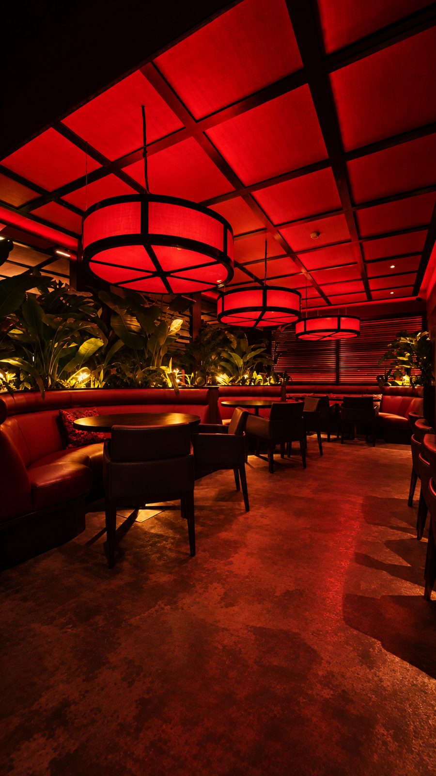 Dining room in red light at Zen with large glowing circular lanterns, banquette seating and tropical planting.
